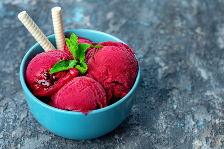Raspberry ice cream in blue bowl on stone table, decorated with several leaves of mint and with waffle sticks.の写真素材