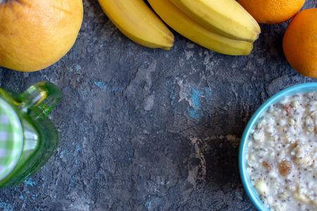 healthy breakfast bowl. oatmeal with banana, raisins, walnuts, chia seeds, jar of drink and fruits on stone backgroundの写真素材
