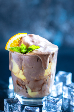 Orange Soda Creamsicle Ice Cream Float in glass decorated with piece of orange and leaves on mint, surrounded by ice cubes on stone table backdropの写真素材
