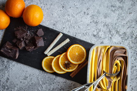 Delicious chocolate and vanilla combo ice cream garnished with fresh orange slices, waffle sticks, cinnamon, bad apple, pieces of chocolate put on shale, white stone backdrop.の写真素材