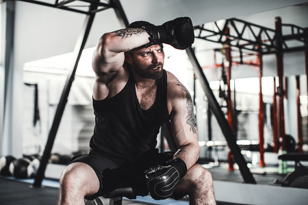 Tired male boxer sitting on stool in gym
