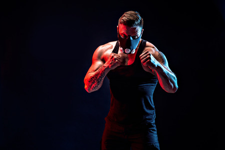 Strong male athlete in a black training mask posing on a black background