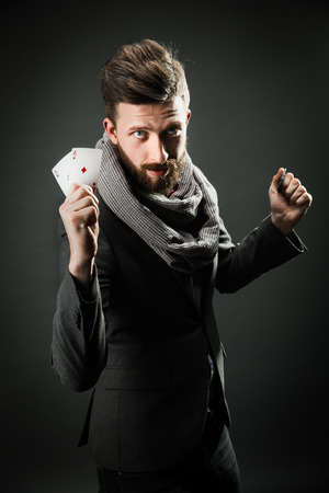 bearded stylish young handsome man holding playing cards in his hands for the casino and looking at the camera emotionally. dark studio backgroundの写真素材