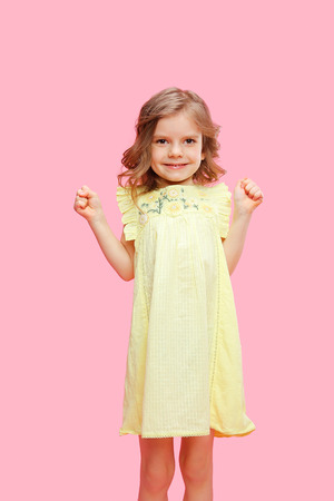 Little adorable model in summer yellow dress posing on pink backdrop in studio.の写真素材