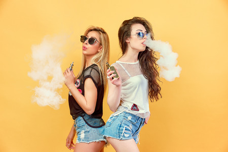 Side view of trendy young female in glasses and shorts standing and smoking on studio backgroundの写真素材