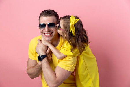 happy fathers day. cute dad and daughter in yellow and sunglasses hugging on colored pink...