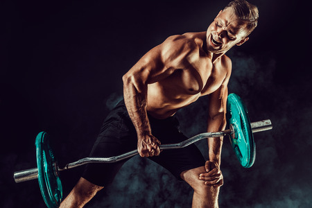 Strong athletic man pumping up muscles workout bodybuilding. muscular bodybuilder handsome men doing exercise for muscles of back with a barbell on dark background with smoke. Strength and motivation.の写真素材