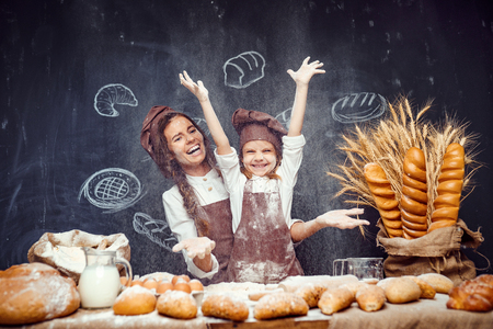 Laughing woman and little girl in aprons of cooks having fun and sprinkling flour in air standing at tableの写真素材