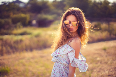 CLose up of a beautiful young woman in dress and sunglasses having fun with hair outdoor in countryside on a warm summer dayの写真素材
