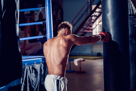 Male boxer training with punching bag in dark sports hall. Young boxer training on punching bag. Male boxer as exercise for the big fight. Boxer hits punching bag.の写真素材