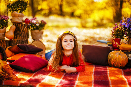 Girl in casual clothes sitting on a checkered red plaid near a basket with apples and flowers in a park. autumn, harvestの写真素材