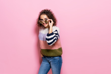 Happy beautiful girl with amazing toothy smile posing in fashionable sweater. Young girl standing on pink pastel background.の写真素材