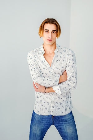 Fashion portrait of young man in white shirt poses over grey wall.の写真素材