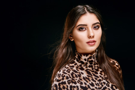 Young alluring woman with waving hair and makeup looking sensually at camera on black backgroundの写真素材