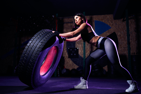 Attractive fit middle age woman athlete working out with a huge tire, turning and flipping in the gym. Crossfit woman exercising with big tire.の写真素材