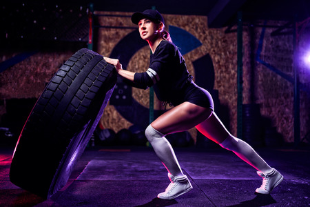 Attractive fit woman athlete working out with a huge tire, turning and flipping in the gym. Cross fit woman exercising with big tire.の写真素材