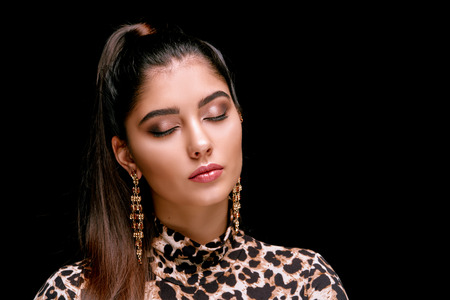 Young alluring woman with waving hair and makeup looking sensually at camera on black backgroundの写真素材