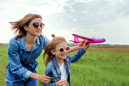 Young woman and girl in denim clothes having fun with small plane on green lawn in summer dayの写真素材