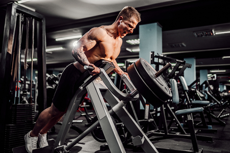 Strong Bodybuilder Doing Heavy Weight Exercise For Back On Machine. T-pull exercise.の写真素材