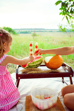 Two smiling girls eats slice of watermelon outdoors on meadow. Mother and daughter spend time together. Diet, vitamins, healthy food concept.の写真素材
