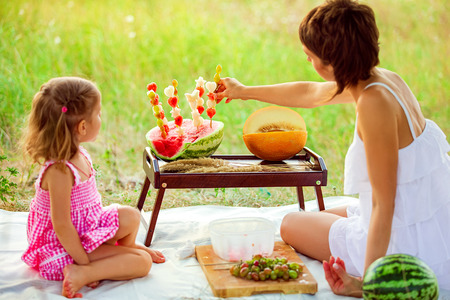 Two smiling girls eats slice of watermelon outdoors on meadow. Mother and daughter spend time together. Diet, vitamins, healthy food concept.の写真素材