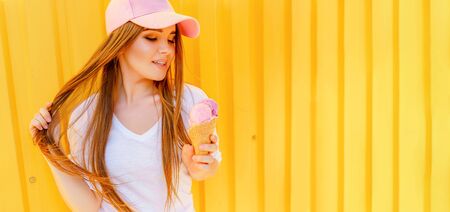 Outdoor fashion portrait of young hipster girl with ice-cream on yellow wall background.の写真素材