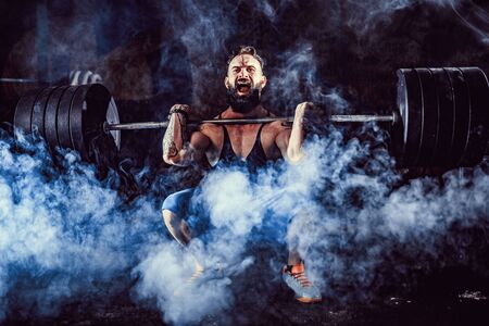 Muscular bearded tattoed fitness man doing deadlift a barbell over his head in modern fitness center. Functional training. Snatch exerciseの写真素材
