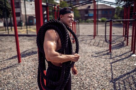 Athletic looking man holding battle rope at street gym yard. Strength and motivation. Outdoor...