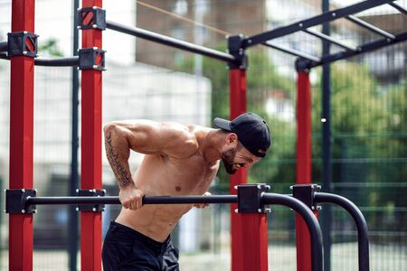 Strong muscular man doing push-ups on uneven bars in outdoor street gym. Workout lifestyle concept.