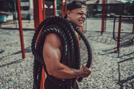 Athletic looking man holding battle rope at street gym yard. Strength and motivation. Outdoor workout.の写真素材