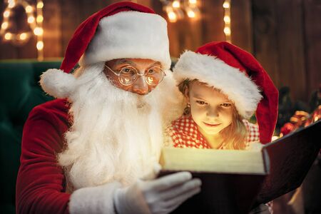 Santa Claus giving a present to a little cute amazed girl in pajama and santa hatの写真素材