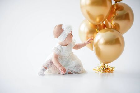 A one year old, baby girl sitting with a bunch of golden balloons on white background in studioの写真素材