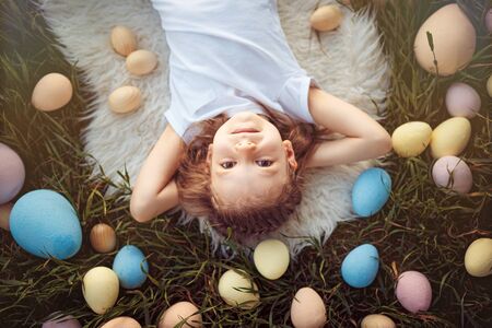 From above young cute girl lying in colorful Easter eggs on green grass