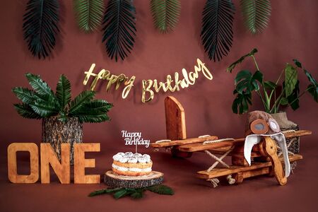 Happy Birthday location for kids with wooden airplane, cake, green tropical plants