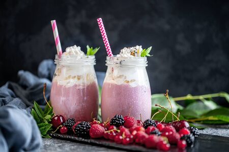 2 jars of milkshake or smoothie with cranberries, strawberries and blueberries standing on stone backdrop.の写真素材