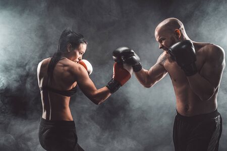 Shirtless Woman exercising with trainer at boxing and self defense lesson, studio, dark background....
