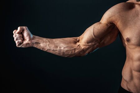 tense arm clenched into fist, veins, bodybuilder muscles on a dark background, isolate.