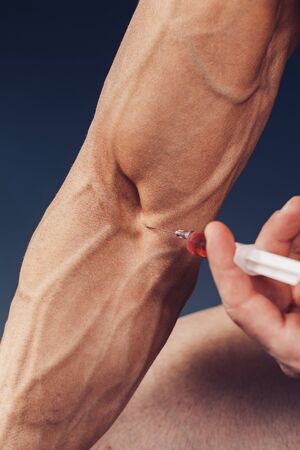 Hand of a muscular man with a syringe. Doing a shot of steroids