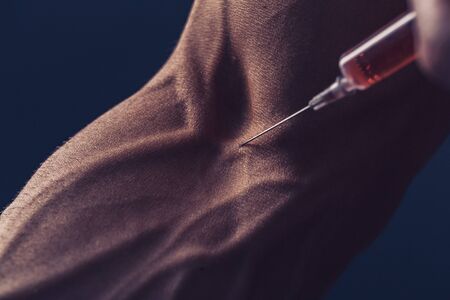 Hand of a muscular man with a syringe. Doing a shot of steroidsの写真素材