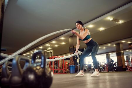 Caucasian fit woman dressed in sportsoutfit doing workout with battle ropes at gym.の写真素材