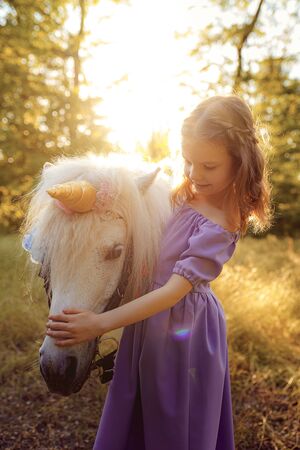 Girl in purple dress hugging white unicorn horse. Dreams come true. Fairy tale.の写真素材