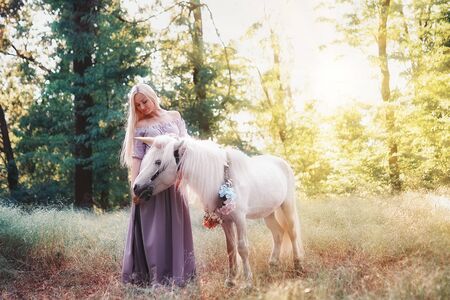 Blonde Woman in purple dress hugging white unicorn horse. Dreams come true. Fairy tale.