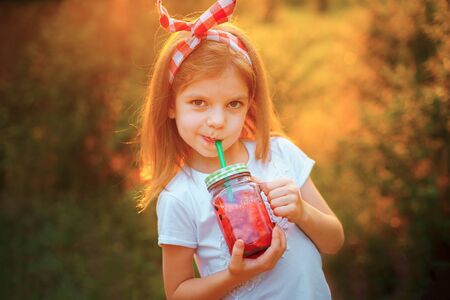 Child drinking Watermelon lemonade in jar with ice and mint as summer refreshing drink. Cold soft...