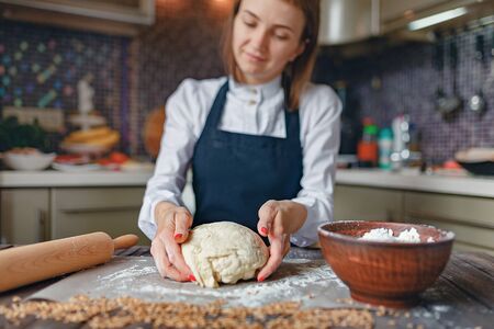 Faceless shot of woman in white shirt and apron flour dough while cooking.