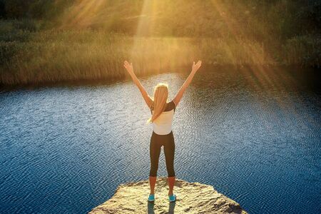Young slim woman practicing yoga outdoors on stone shore of mountain river. Unity with nature...