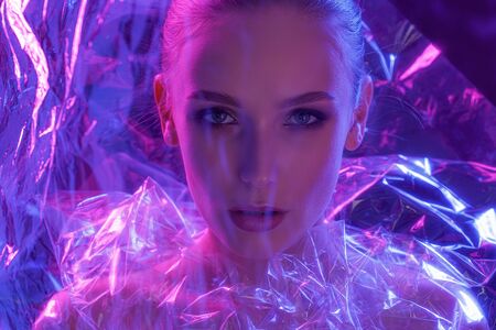 High Fashion model girl in colorful bright neon lights posing in studio through transparent film....