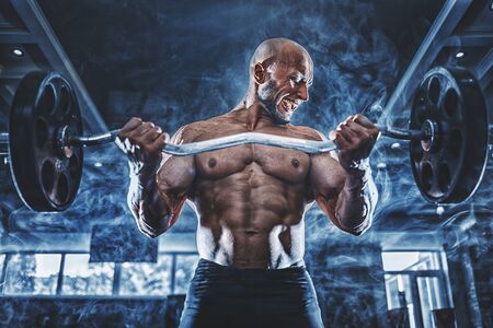 Muscular man working out in gym doing exercises with dumbbells at biceps, strong male naked torso abs in smoke.の写真素材
