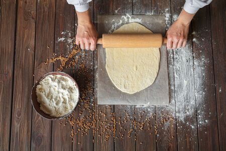 Womans hands roll out the dough on a tableの写真素材
