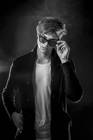 Trendy young man with cool hairstyle wearing black jacket with sunglasses. High Fashion male model posing on black background. Art design conceptの写真素材