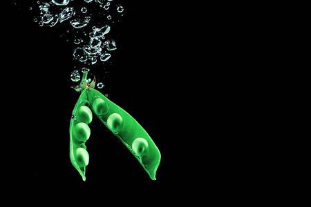 Fresh pea dropped into a water on dark background isolate.の写真素材